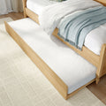 Wooden trundle bed with pull-out underbed drawer, white bedding and light blue throw on a textured cream rug