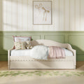 Cozy pastel nursery: cream daybed with floral pillows and teddy bear, sage green wainscoting, striped floral wallpaper and framed bow artwork