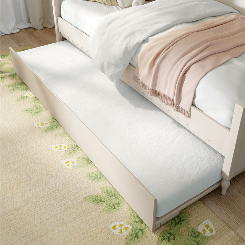 Space-saving white trundle bed pulled out from under a cream wooden twin bed with white bedding, blush pink throw and floral area rug