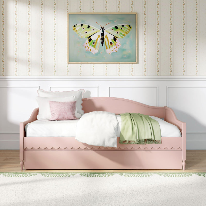 Pink daybed with white bedding and green throw in a pastel girl's bedroom featuring framed butterfly wall art and floral striped wallpaper