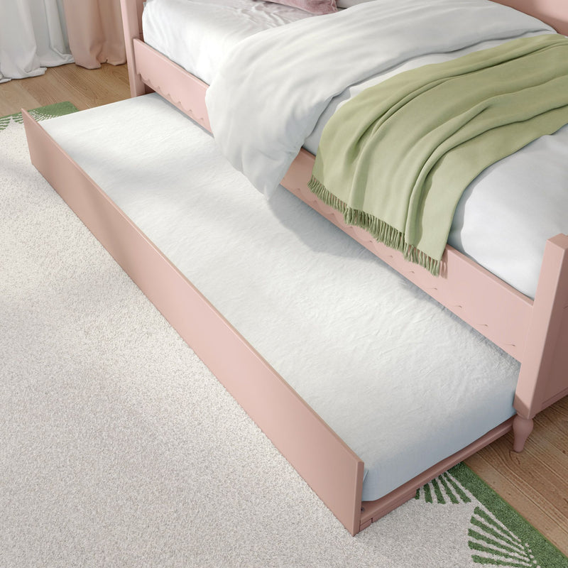 Pink wooden trundle bed with pull-out mattress, white bedding and sage green throw blanket on hardwood floor in a kids' bedroom