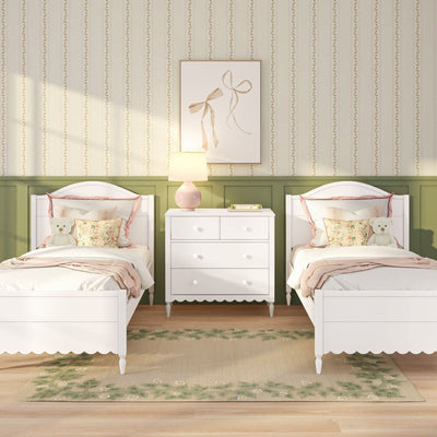 Children's twin bedroom with white beds, green wainscoting, floral striped wallpaper, white dresser, pink lamp, floral pillows and teddy bears