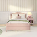 Cozy pastel girls' bedroom with pink scalloped bed, white pillows, green throw, striped floral wallpaper and pink nightstand with lamp