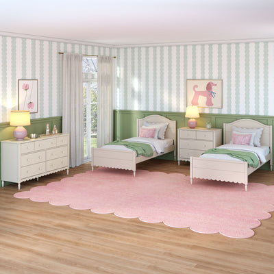 Children's pastel twin bedroom with white beds, pink scalloped rug, green wainscoting, striped wallpaper, floral and poodle wall art, dresser and bedside lamps