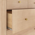 Close-up of light maple dresser with partially open drawer, brass knobs, visible wood grain and metal drawer slide