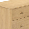 Close-up of modern light pine dresser with natural wood grain finish, smooth rounded top edge and brass drawer knob.