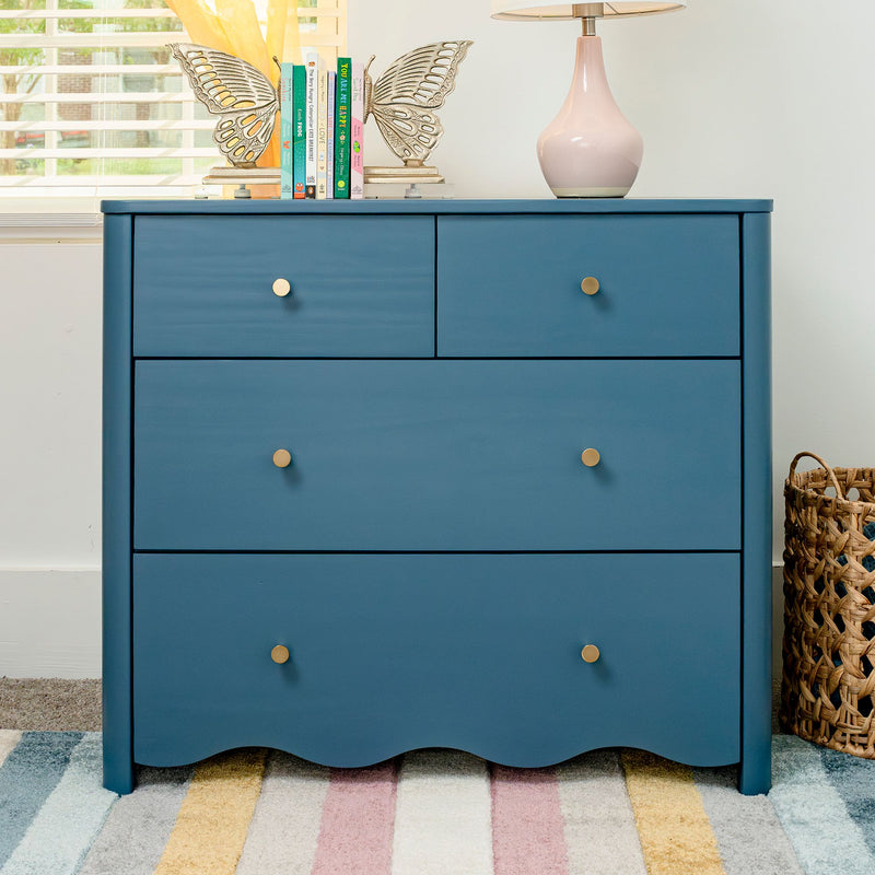 Modern teal blue dresser with brass knobs, butterfly bookends holding children's books, pink table lamp and woven basket on a striped pastel rug