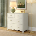 White three-drawer dresser with brass knobs in modern nursery or bedroom setting, styled with green ceramic lamp, vintage radio, framed duck art, and gold floor lamp