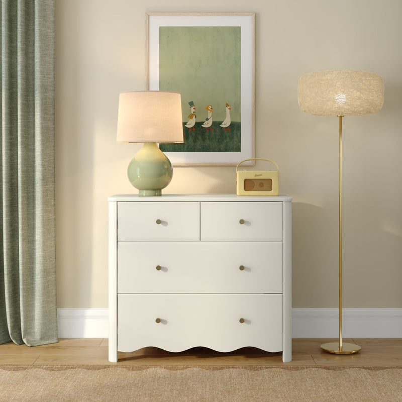 White dresser styled with green ceramic table lamp, framed duck artwork, vintage yellow radio, gold floor lamp and green curtain