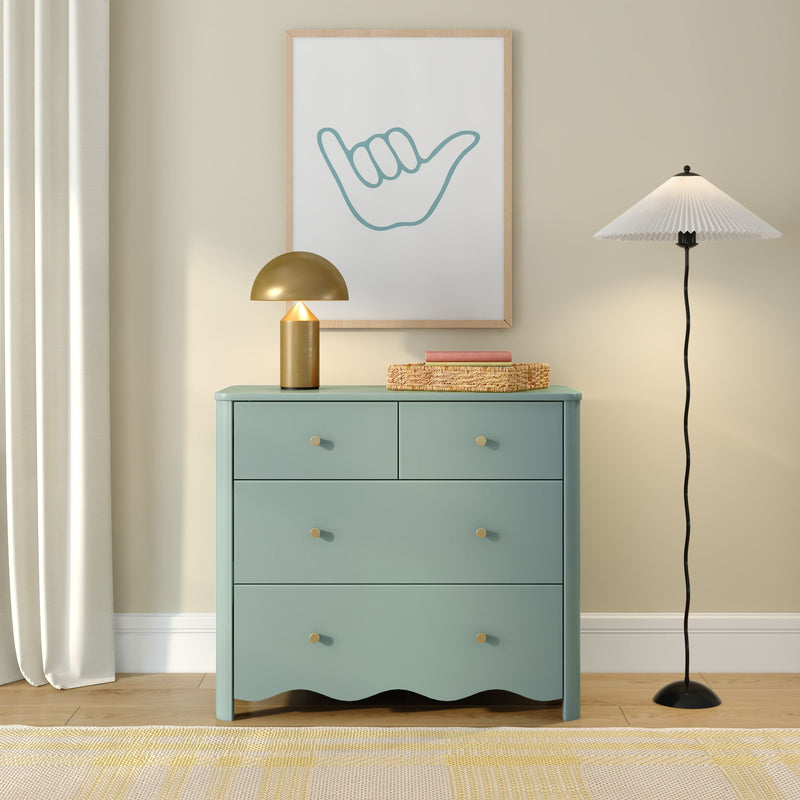 Modern minimalist interior with mint green chest of drawers, gold dome table lamp, pleated floor lamp, woven basket and framed shaka hand artwork on a beige wall
