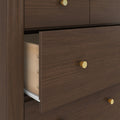 Close-up of a dark walnut dresser drawer partially open showing light wood dovetail joints, metal drawer slides and round brass knobs