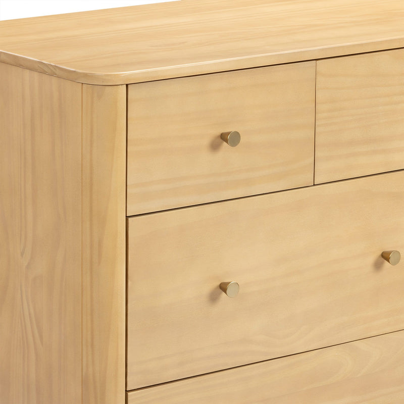 Close-up of light natural wood dresser with smooth rounded top edge and brass cone drawer knobs, modern minimalist chest of drawers