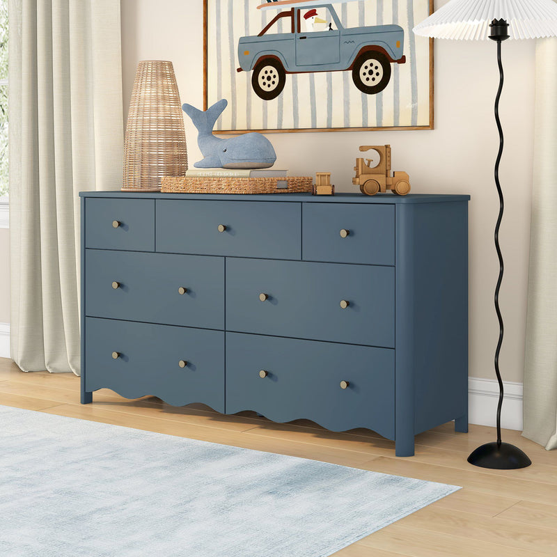 Blue wooden nursery dresser with multiple drawers and brass knobs in children's bedroom, scalloped base, toy storage and coastal kids room decor