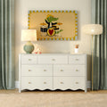White six-drawer nursery dresser with lamp, giraffe toy, pencil holder and crocodile drummer wall art, green curtains