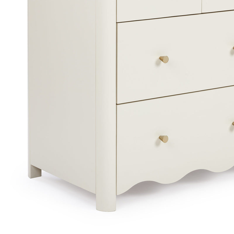 Close-up of cream three-drawer wooden nightstand with matte finish, gold brass cone knobs and scalloped apron, modern bedroom storage furniture