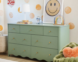 Green kids dresser in nursery with white table lamp, blue alarm clock, wooden bead toy and framed smiley wall art with orange polka-dot decals — children's room storage and decor