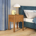 Wooden nightstand bedside table with drawer, white dome lamp and yellow instant camera next to blue upholstered bed in modern bedroom