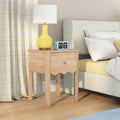 Light-wood bedside table (nightstand) with drawer, yellow ceramic lamp and blue flip alarm clock next to upholstered bed with white pillows and yellow bedding — modern bedroom decor on hardwood floor