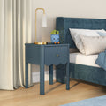 Blue nightstand with gold table lamp and smiling succulent planter next to teal upholstered bed on light hardwood floor, modern bedroom decor