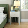Modern bedroom nightstand with white bedside table, green glass lamp, blue flip alarm clock, yellow water bottle beside green upholstered bed, gray curtains and wood floor