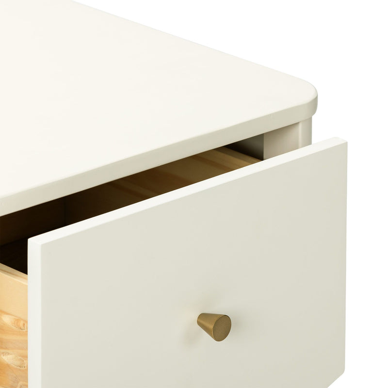 Close-up of cream-painted wooden dresser with a partially open drawer and brass cone knob, minimalist bedroom storage