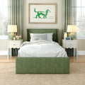Green upholstered twin bed in cozy modern bedroom with white nightstands and table lamps, striped bedding and gingham pillow, green curtains, framed watercolor dog art above bed, natural light from windows