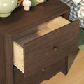 Dark walnut wooden nightstand with open drawer and brass knobs, bedside lamp and mushroom decor on hardwood floor next to checkered bedding, modern bedroom furniture