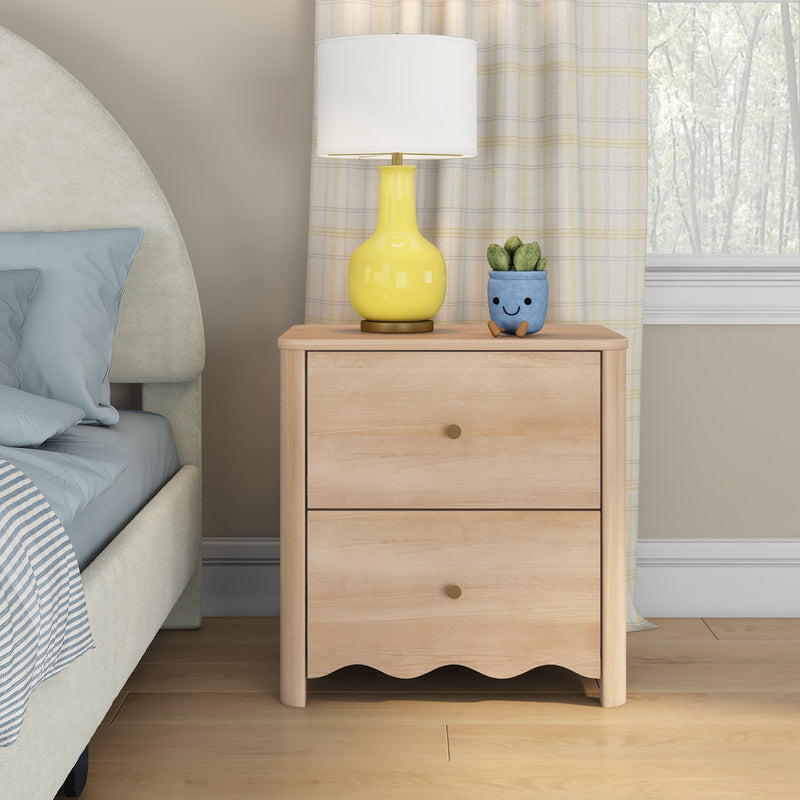 Light wood two-drawer nightstand beside upholstered bed with yellow ceramic table lamp and small blue succulent pot, cozy neutral bedroom decor