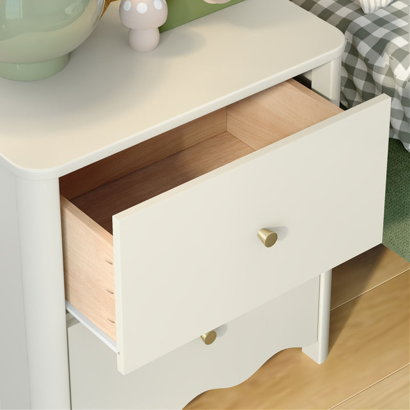 White nightstand with open drawer revealing wooden interior, brass knobs, green décor and checkered bedding