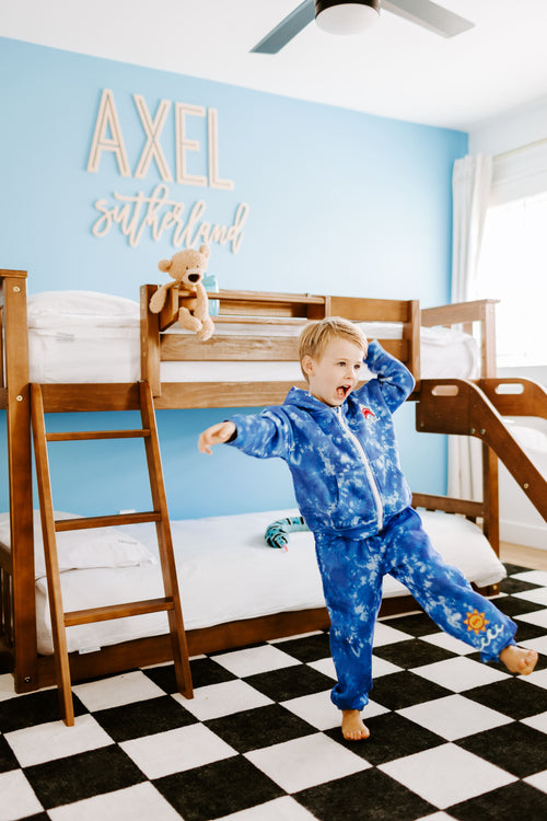 Child in pajamas standing in a bedroom with bunk beds and a blue wall.