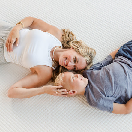 Smiling mother and son lying on a white mattress, testing a comfortable family mattress in a bright bedroom