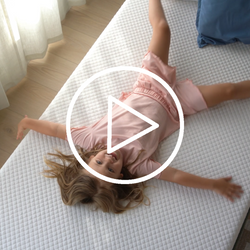Child happily playing on a comfortable mattress in a sunlit bedroom.
