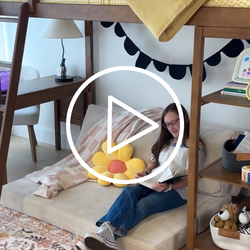 Girl reading a book under a loft bed in a cozy children's room with stylish decor.