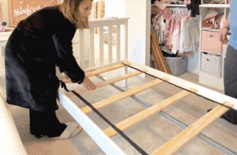 People assembling a white bunk bed frame in a floral-themed bedroom.