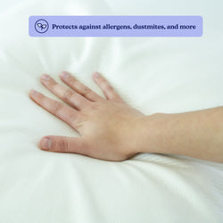 Hand pressing down on a white mattress protector that provides protection against allergens and dust mites.
