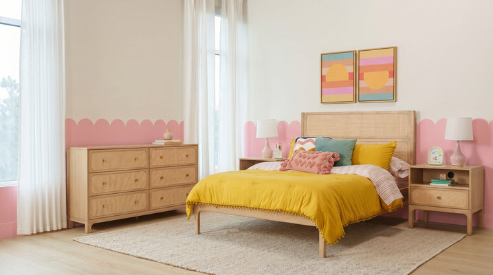 Modern pastel bedroom with scalloped pink wall trim, rattan bed and dresser, mustard yellow duvet, textured pillows, abstract sunset prints and sheer curtains