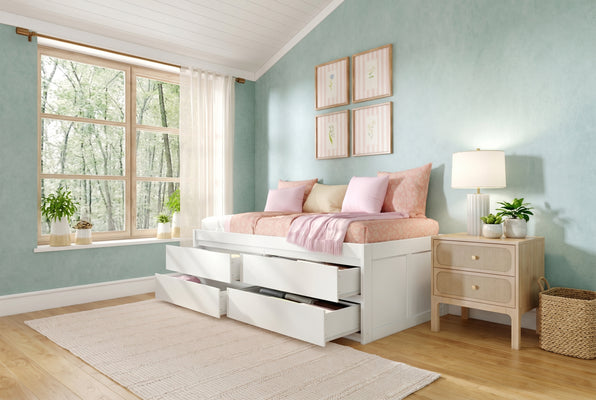 White storage bed with multiple under-bed drawers, pastel pink bedding and throw, mint green textured walls, large wood-frame window with sheer curtains, bedside nightstand, lamp and potted plants for small bedroom storage and decor ideas