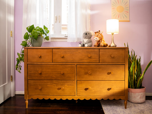 Mid-century wooden dresser styled for nursery decor with table lamp, potted plants (pothos, snake plant) and plush koala and giraffe toys