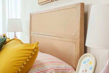 Woven rattan headboard with yellow pom-pom cushion, striped sheets and bedside lamps in a modern boho bedroom