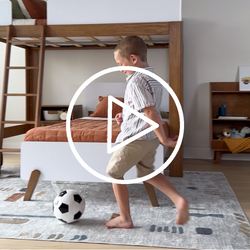 Child playing with a soccer ball in a cozy bedroom with a bunk bed and soft rugs.