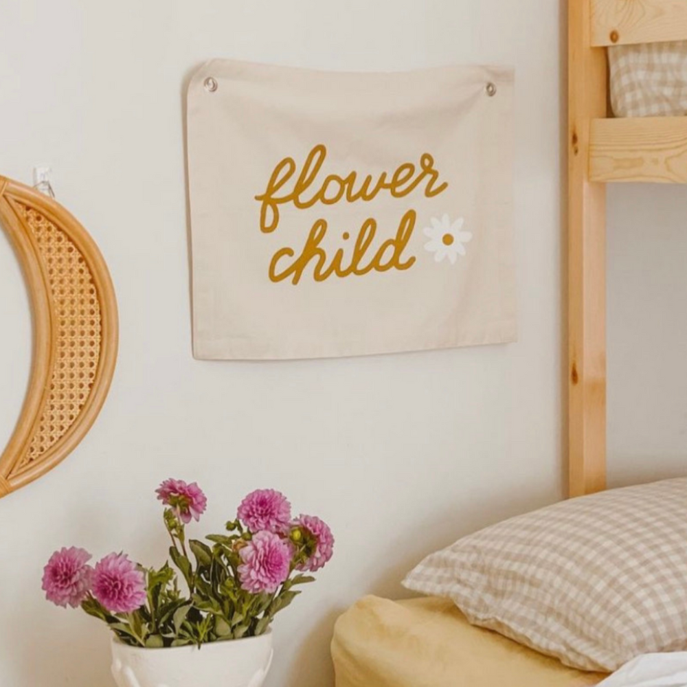 Cozy bedroom decor with a "flower child" wall hanging and a vase of vibrant pink flowers.