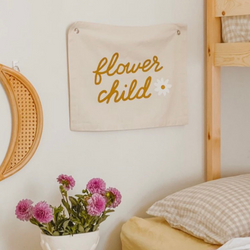 Cozy bedroom decor with a "flower child" wall hanging and a vase of vibrant pink flowers.