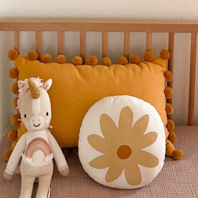 Stuffed unicorn toy and decorative mustard yellow pillows on a wooden crib.