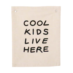 Decorative beige wall hanging with the phrase 'Cool Kids Live Here' in bold black text, ideal for children's room decor.