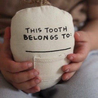 Child holding a tooth fairy pillow with "This tooth belongs to" inscription, perfect for preserving children's lost teeth.