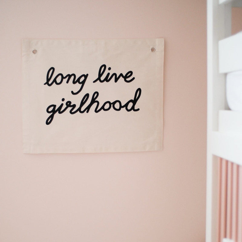 Wall banner with the inscription 'long live girlhood' on a peach background, promoting girl empowerment and positivity.