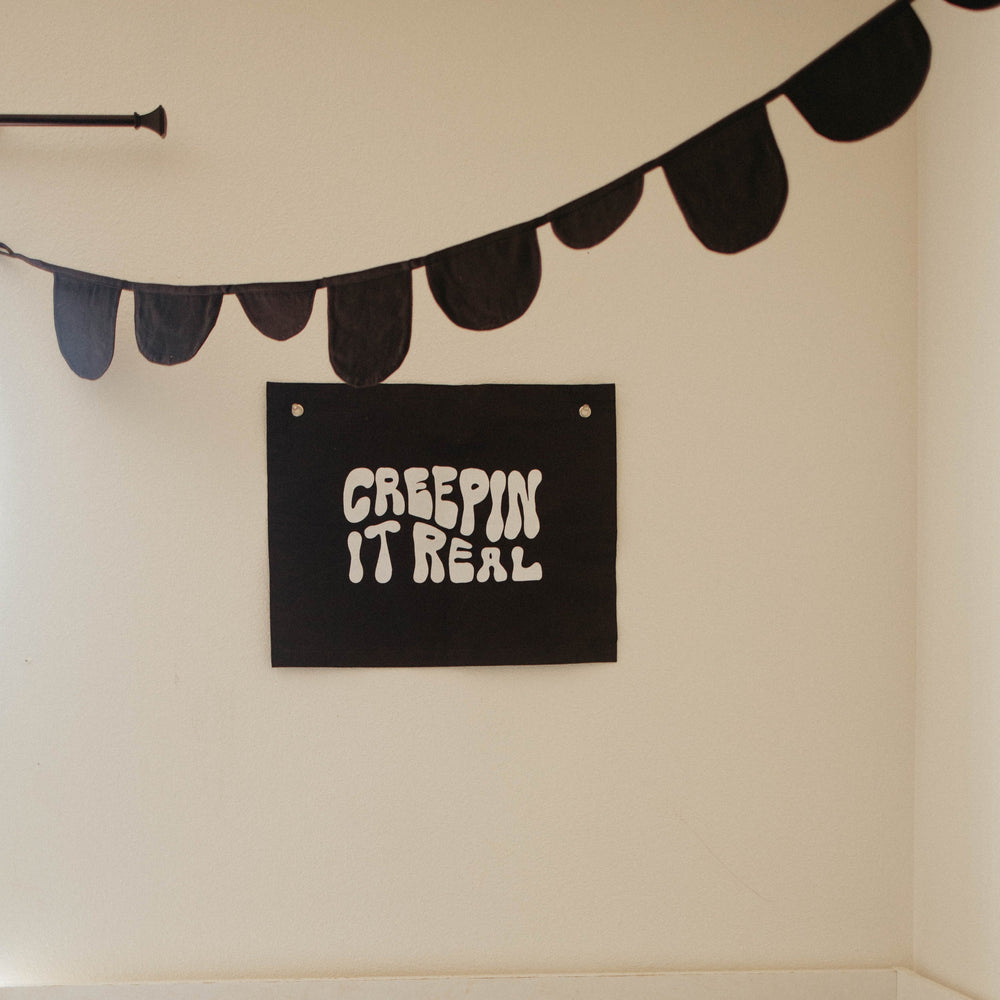 Black Halloween wall decoration with "Creepin It Real" sign and black bunting banner.