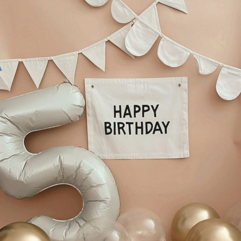 Happy birthday party decorations with large metallic number 5 balloon and festive white and gold balloons.