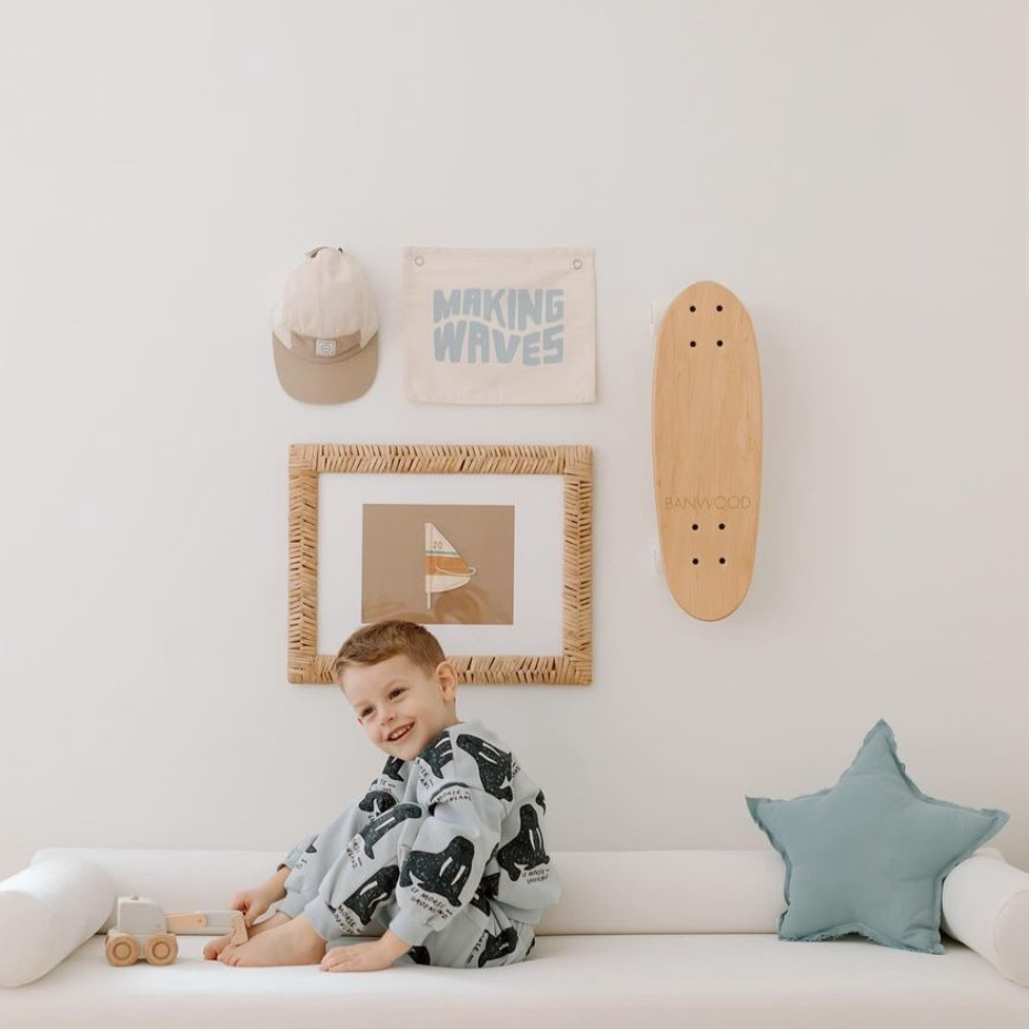 Child sitting on a white couch in a playful bedroom with a skateboard and wall art.