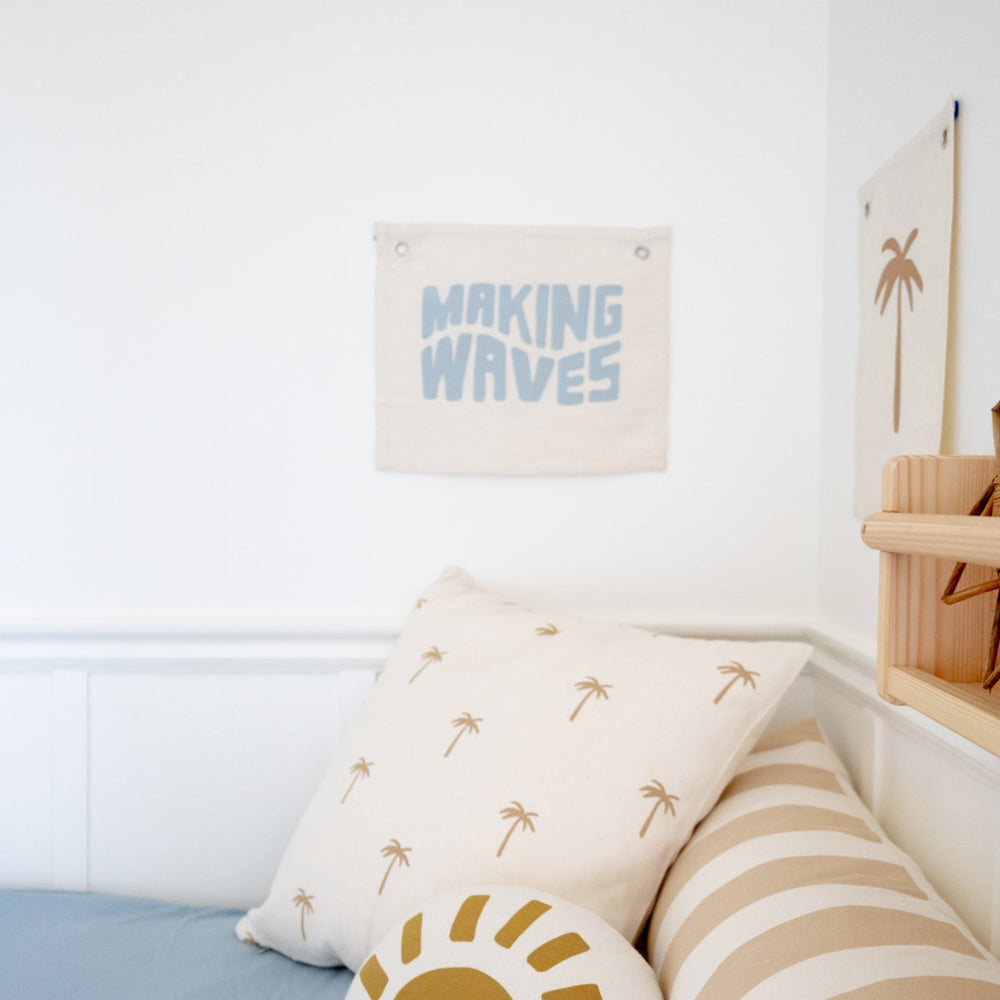 Cozy nautical-themed bedroom decor with "Making Waves" wall art and palm tree patterned cushions.